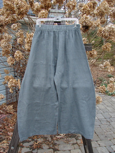 A close-up of Barclay Linen Crop Side Pocket Pant in Dusty Sky, a light-weight linen pant with a billowing fall and vertical sectional panels. Features a thicker elastic waistline and two upper hip front pockets. Size 0.