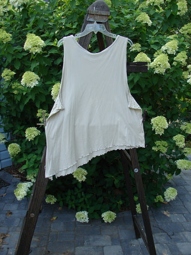 Barclay Batiste Curly Seam Tank Rain Sand Size 2 displayed on a clothes rack outdoors, showcasing its asymmetrical hem and curly edgings, with plants visible in the background.