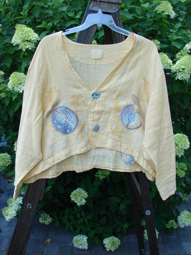 Yellow linen Weathervane Jacket with unique front buttons, deep V-neck, inward rounded side hem, and summer fruit theme paint, displayed on a wooden stand. Spring Collection 1999, Buttercup, Size 2.