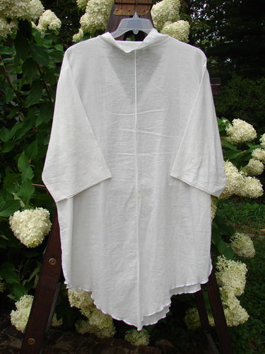 Barclay Batiste Flutter Tunic Top Unpainted White Size 3 displayed on a hanger, featuring a V neckline, flutter collars, drop shoulders, and three-quarter length sleeves with soft exterior stitchery.