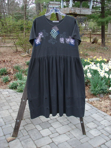 1996 Constellation Dress Garden Path Storm Size 2 hanging on a rack, featuring a creatively accented adjustable hemline, continuous loops, rear buttons, and a garden path theme painted on mid-weight organic cotton.