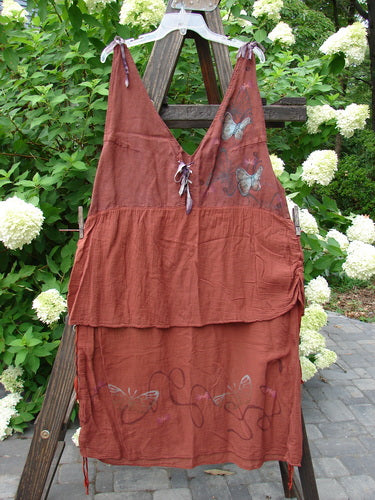 Barclay Gauze Linen Two Tier Ribbon Jumper Butterflies Cinnabar Size 1 displayed on a wooden structure, showcasing deeper arm openings, silk ribbon ties, lace-up front, and an empire waist with butterfly theme.