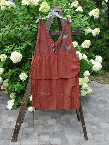 Barclay Gauze Linen Two Tier Ribbon Jumper Butterflies Cinnabar Size 1 displayed on a wooden rack, showcasing deep V-neckline, empire waist, silk ribbon ties, and lace-up front bodice.