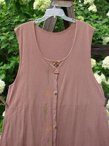 1993 Sleeveless Jumper Vest Sweet Pea Dried Rose OSFA: A brown shirt and a pink shirt on clothes racks, with a plastic object on a wood surface.