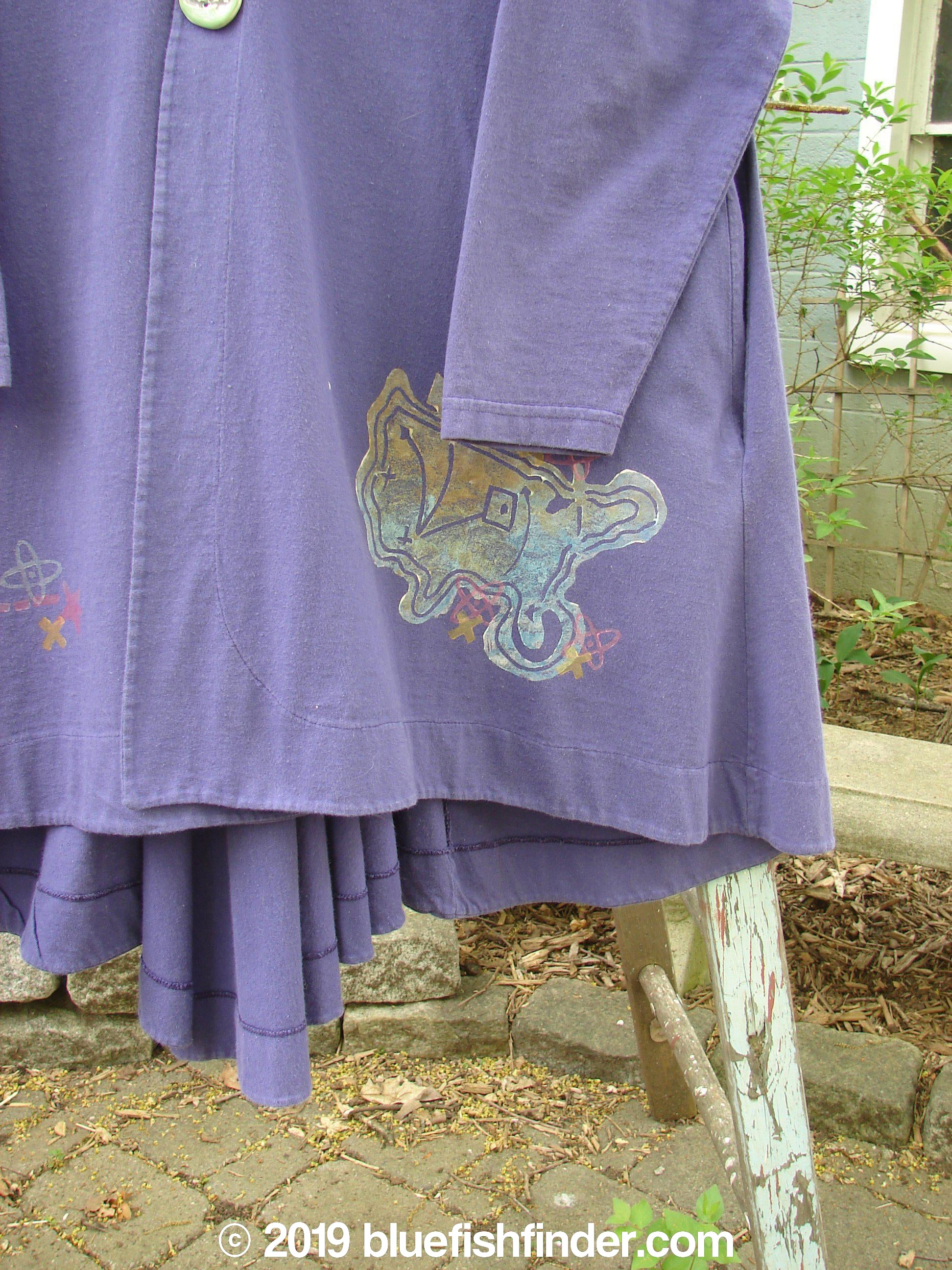 1996 Dining Car Jacket Travel Niagara Size 1: A purple robe-like jacket made from organic cotton. Features include a V-shaped neckline, artisan porcelain buttons, and a travel-themed paint design.