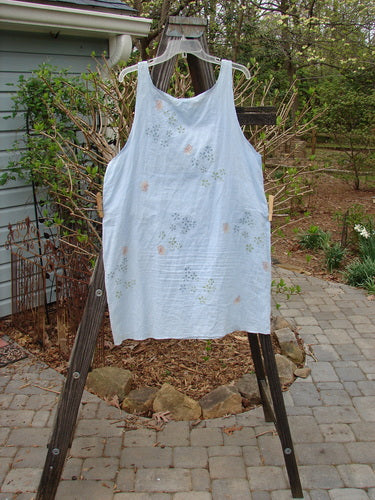 A white shirt with a floral theme paint on it, displayed on a wooden ladder.