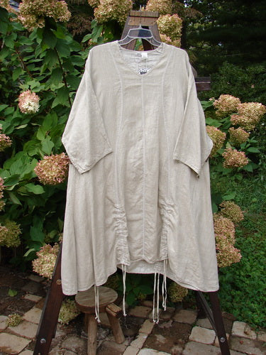 Barclay NWT Linen Shimmer Venetian Tunic Dress Unpainted Sand Shell Size 2 displayed on a wooden swing, highlighting its generous shape, pinched sleeves, and softly rounded V-shaped neckline.
