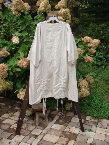 Barclay NWT Linen Shimmer Venetian Tunic Dress Unpainted Sand Shell Size 2 displayed on a wooden swing, showcasing its generous shape, softly rounded V neckline, and vertical draw cords.