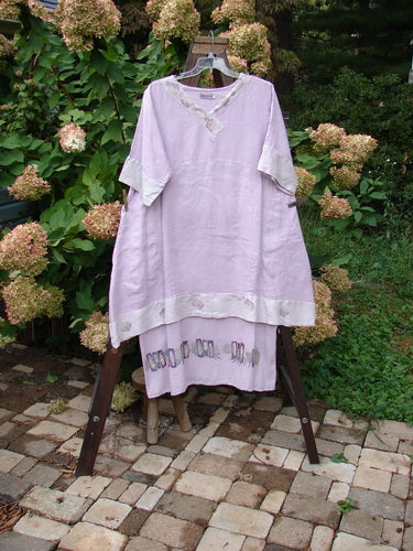 Barclay Linen Crossover Two Tier Dress Floral Lavender Size 2 displayed on a clothes rack, showcasing its V neckline, wide cuffs, double-layered flow, and floral pattern.