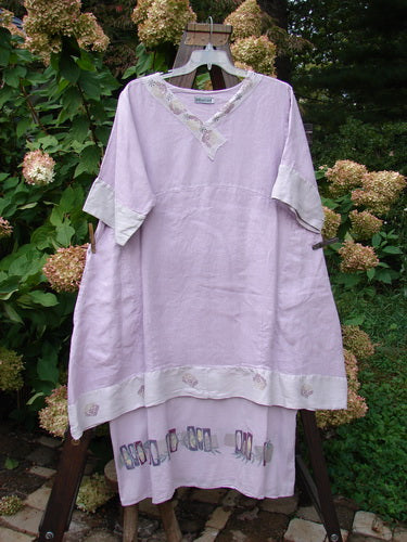 Barclay Linen Crossover Two Tier Dress in Floral Lavender Size 2 displayed on a swing, showcasing its V-neckline, double-layered flow, wide cuffs, and floral theme.