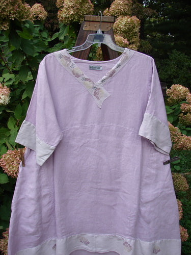 Barclay Linen Crossover Two Tier Dress Floral Lavender Size 2 displayed on a wooden hanger, showcasing its V neckline, double-layered flow, and contrasting lower sleeves with wide cuffs.