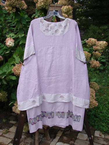 Barclay Linen Crossover Two Tier Dress Floral Lavender Size 2 displayed on a swing, featuring a V neckline, contrasting sleeves, and double-layered flow, emphasizing its floral theme and elegant design.
