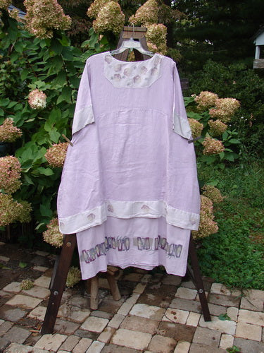Barclay Linen Crossover Two Tier Dress Floral Lavender Size 2 displayed on a swing, showcasing its V neckline, double-layered flow, and wide cuffs in an outdoor setting.