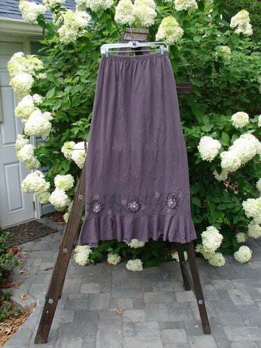 1996 Spring Laughter Skirt Vine Blossom Violet Field Size 2 displayed on a wooden stand with a backdrop of white flowers, highlighting its full elastic waistband and detailed vine blossom theme.