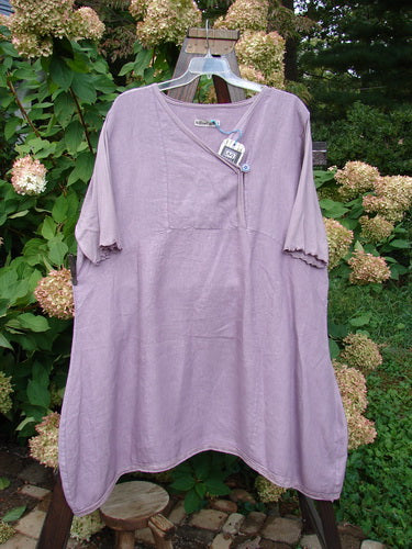 Barclay NWT Linen Lace Blooming Tunic Dress Unpainted Lavender Size 2 displayed on a hanger, showcasing its cross-over neckline, empire waist seam, lace-trimmed hem, and three-quarter scallop-edged sleeves.
