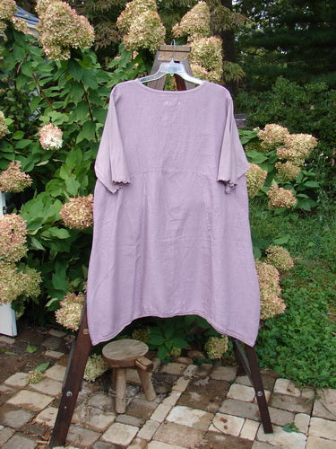Barclay NWT Linen Lace Blooming Tunic Dress Unpainted Lavender Size 2 displayed on a swing with a wooden stool underneath, highlighting the cross-over neckline, lace-trim hem, and scallop-edged sleeves.