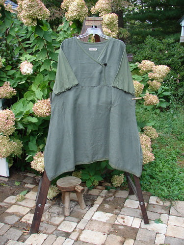 Barclay Linen Lace Blooming Tunic Dress Unpainted Army Size 2 displayed on a rack, featuring a cross-over neckline, empire waist, lace hem trim, and three-quarter scallop-edged sleeves.