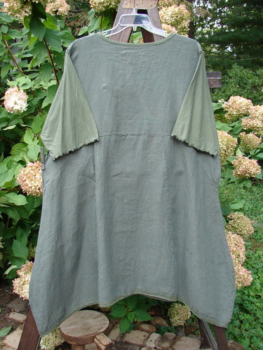 Barclay Linen Lace Blooming Tunic Dress Unpainted Army Size 2 displayed on a clothes rack, showcasing a cross-over neckline, empire waist, lace trim hem, and scalloped three-quarter sleeves.