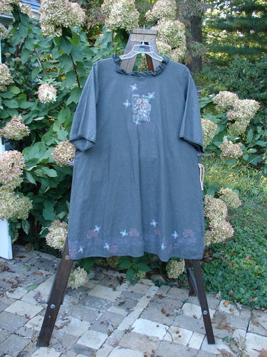 Barclay Linen Duet Sunrise Dress in Stormy Grey, size 2, displayed outdoors. Features a floral graphic, empire waistline, puckered pleats, and painted pockets, embodying vintage Blue Fish Clothing's creative freedom.