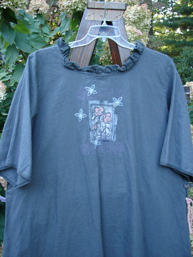 Barclay Linen Duet Sunrise Dress in Stormy Grey, featuring a ruffled collar and a small rose graphic within a window frame, hangs outdoors on a clear hanger, capturing its unique texture.