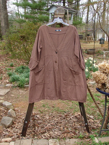 Barclay Linen Adras Uptown Jacket Unpainted Redwood Size 0 displayed on a swing, showcasing its deep V-neckline, pleated sleeves, and double exterior front pockets.