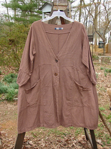 Barclay Linen Adras Uptown Jacket Unpainted Redwood Size 0, displayed on a clothes rack, showcasing a deep V-shaped neckline, pleated banded sleeve, double front pockets, and sectional triangular panels.