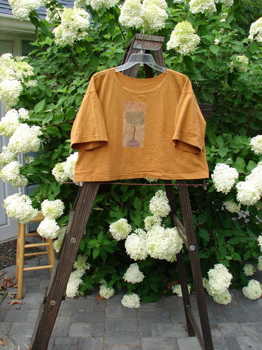 1994 Short Sleeved Boxy Tee Top Topiary Dijon OSFA: A shirt on a swinger with white flowers, a wooden stool with a flower, and a yellow shirt with a picture on it.