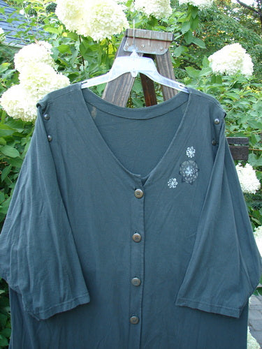 1994 Convertible Coat Spin Flower Deep Moss OSFA displayed on a hanger outdoors, showcasing its unique button-on/off sleeves for versatility, scooped front hemline, and distinctive flower theme paint details.