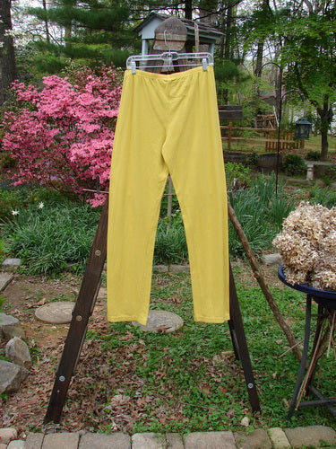 Barclay NWT Cotton Lycra Bally Layering Pant Legging in Goldenrod. A pair of yellow pants on a rack in a backyard, with a close-up of a plant and a metal pole.