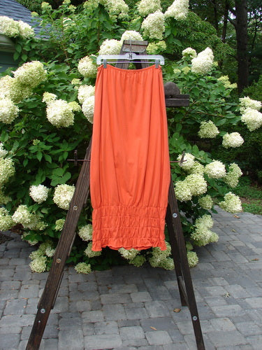 2000 Rings of Saturn Skirt Unpainted Fire Size 2 on a rack, showcasing its full skinny larger elastic waistline, tapered lower, and detailed stretchy smocking, made from lightweight organic cotton.