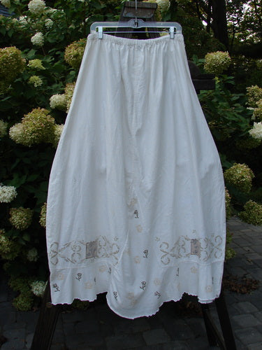 Barclay Linen Duet Skirt Tiny Floral White Size 2 hanging on a clothesline, showcasing its full elastic waistline, widening bell shape, sectional panels, front V-shaped insert, varying hemline, and tiny floral design.