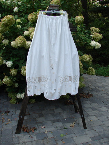 Barclay Linen Duet Skirt Tiny Floral White Size 2 displayed on a rack, showcasing its full elastic waistline, bell shape, sectional panels, V-shaped insert, varying hemline, and tiny floral theme paint.