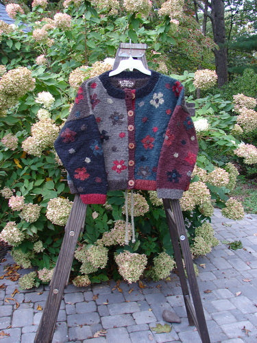 Tara Handknits Box Tie Back Cardigan Sweater Tiny Floral OSFA hanging on a rack outdoors, showcasing intricate patterns, oversized round buttons, and ribbed cuffs and hem.