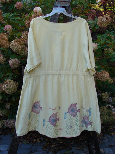Barclay Linen Flower Button Gather Back Tunic Dress: A white dress with a fish design, featuring a full pearly button flower front, an A-line shape, and a rounded hemline. Slightly longer short sleeves and an elastic drop waistline in the rear. Made from medium weight linen. Size 2.
