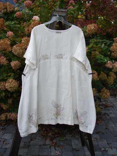 Barclay Linen Urchin Tunic Dress Undersea White Size 2 displayed on a mannequin, showcasing its A-line shape, wide short sleeves, and downward curved empire waist seam, with a floral design in an outdoor setting.