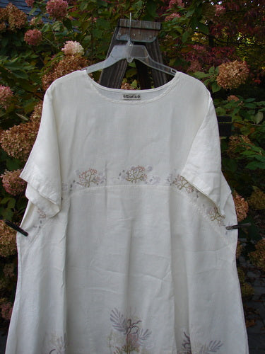 Barclay Linen Urchin Tunic Dress Undersea White Size 2 displayed on a metal hanger, featuring a rounded neckline, wide short sleeves, and a downward curved empire waist seam.