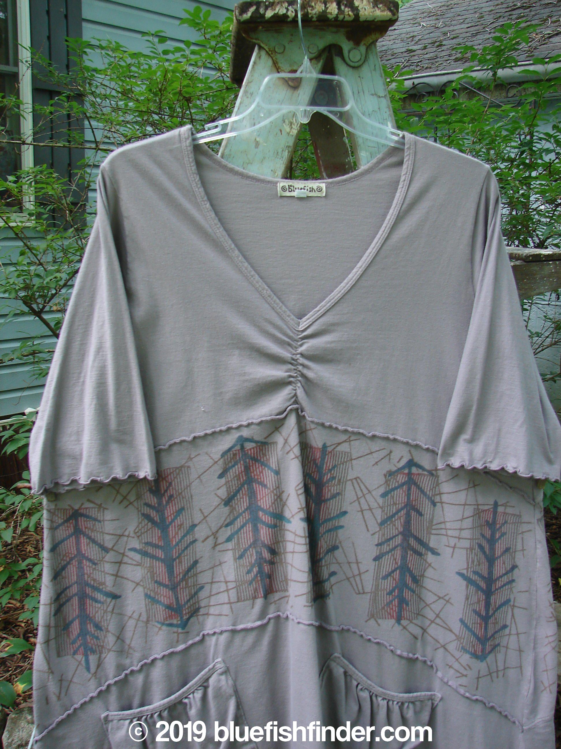 A Barclay Cotton Lycra Vertical Gather Drop Pocket Dress in Pine Forest Grey Stone. Features include a V-shaped neckline, varying hemline, oversized front pockets, and lovely pine forest paint.