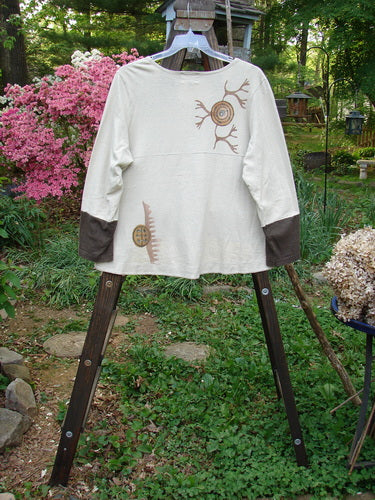 A white jacket with brown designs on it, part of the 2000 Cotton Hemp Philois Jacket Bio Dove Bark Size 1 collection. Features include a scooped varying hemline, sectional horizontal panels, contrasting sleeves, two lower pockets, taganut number buttons, rear flounce, and a gently rounded neckline.