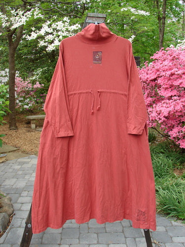 1995 Omega Dress Triple Path Red Glaze Size 1 displayed on a pole, showcasing a ribbed turtleneck, drop shoulders, deep side pockets, and a flared A-line with a drawcord backline.