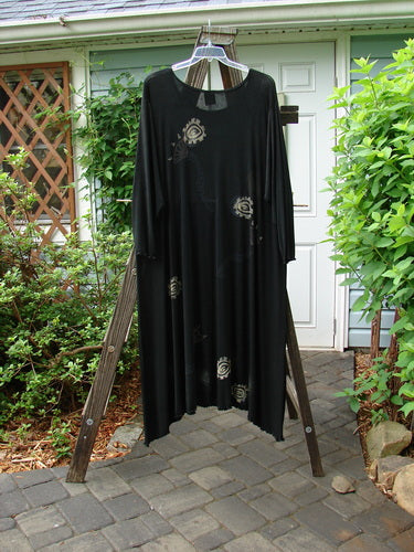 1995 Acetate Lycra Celebration Dress Celtic Turn Onyx Size 2 hanging on a wooden rack, featuring a sweeping lettuce-edged varying hemline and slightly longer sleeves.