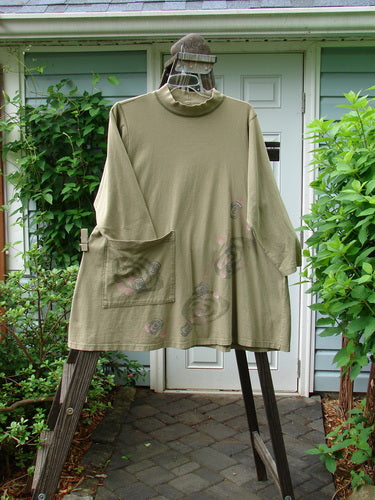 1996 Rambler Dress Follow Path Bottlecap Size 1 on a hanger, featuring a ribbed mock T-neck, A-line shape, oversized front pocket, side pocket, and exterior stitching, displayed outdoors.