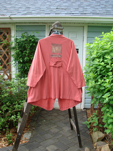 A close-up of a pink shirt with a pocket on a wooden fence.
