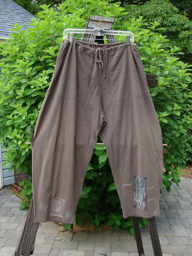 1994 Wanderer's Pant Spirit Woman Humus Size 1 displayed on a clothes rack, featuring a cropped length, full drawstring waist, side entry front pockets, and widening rounded hip with a unique cactus design.