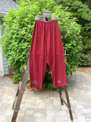 1997 Simple Pant Love Dove Regalia Size 1: A pair of red pants on a wooden ladder, with a clothes line and wooden rack nearby.