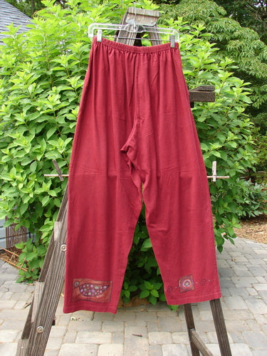 1997 Simple Pant Love Dove Regalia Size 1: A pair of red pants on a clothes rack, featuring a love dove theme paint design. Made from organic cotton, these pants have a full elastic waistband, two deep side pockets, and a slightly straighter fall. Perfect condition.
