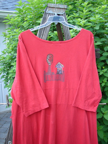 A red shirt with a drawing of a house and a tower, featuring a deep V-shaped neckline, flat tape lacings, and three-quarter length sleeves.