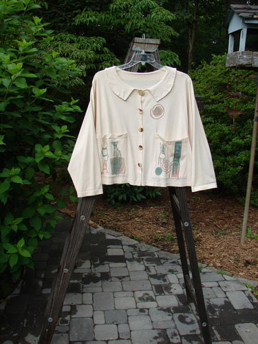 1994 Box Pocket Jacket Mixed Letter A Ecru Size 2, featuring a unique collar, large painted front pockets, and vintage buttons, displayed on a rack.