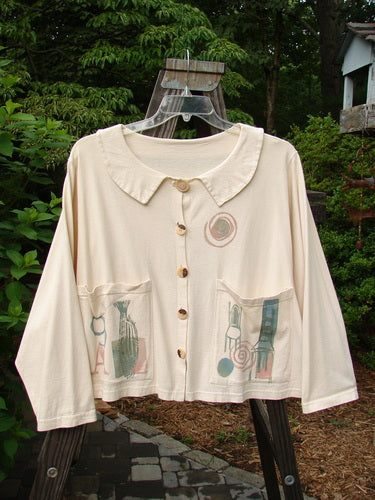 1994 Box Pocket Jacket Mixed Letter A Ecru Size 2, featuring a unique collar, two large front pockets, oversized buttons, and a cropped boxy shape with vintage-themed paint, displayed on a wooden stand.