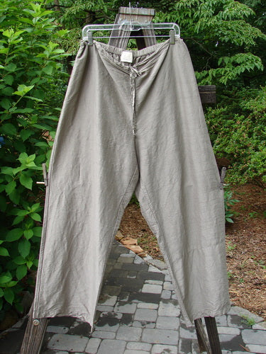 2000 Shaunting Silk Slant Drawcord Pant Cement Size 2: A pair of pants on a clothes rack from the Transitions Collection. Rear elastic waistband with drawcord front. Wider hips and lowers. Classic Transitions theme paint. Longer inseam and full length. Waist relaxed 26 to 56. Waist extended 56. Hips 56. Inseam 26. Length 40 inches.