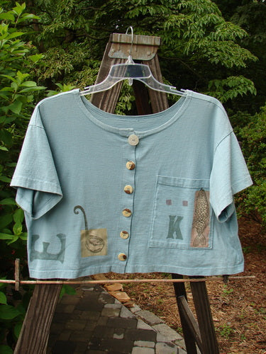 1994 Song Top Multi Letter "K" Ice Size 1: A wide, boxy blue shirt with a fish design on it. Features include a shallow neckline, vintage buttons, and a painted breast pocket.